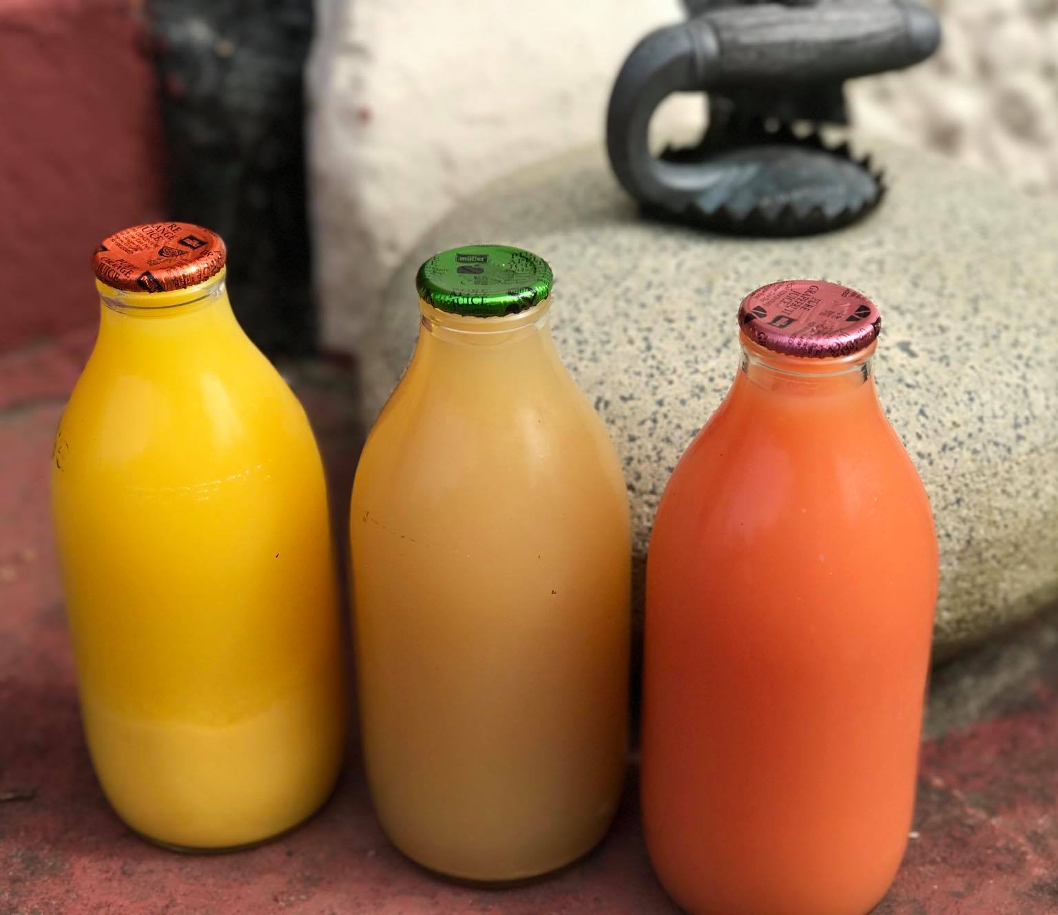 Three glass bottles of juice on a doorstep — orange, apple, and grapefruit